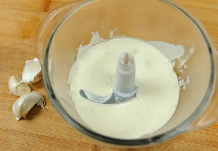 Crème d'ail onctueuse dans un mixeur, prête à être dégustée. Quelques gousses d'ail frais à côté.
