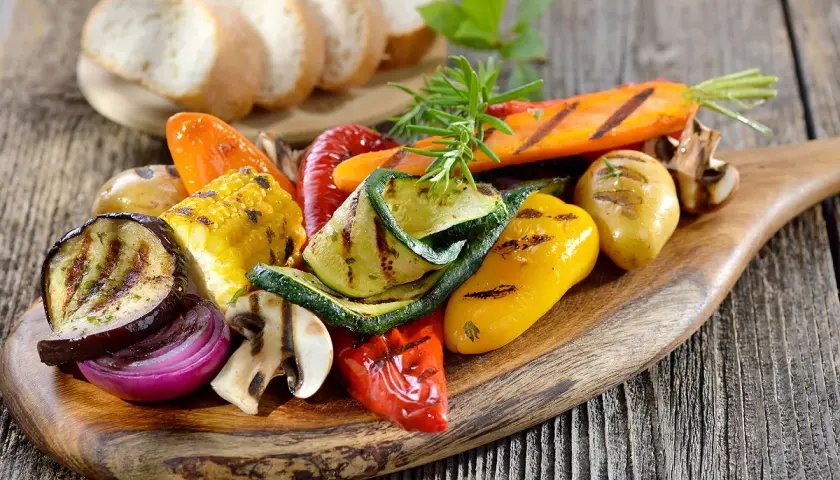Légumes grillés colorés sur une planche en bois, accompagnés de pain frais. Un filet de crème de balsamique sublimerait ce plat.