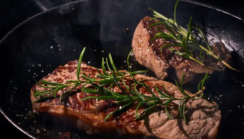 Deux steaks de boeuf Black Angus savoureux, poêlés avec du romarin et du gros sel, dégageant une vapeur alléchante.