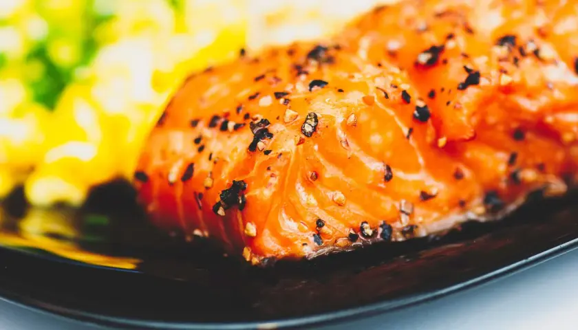 Un délicieux filet de saumon, assaisonné de poivre, prêt pour un barbecue de la mer. Accompagné d'une purée verte et jaune floue.