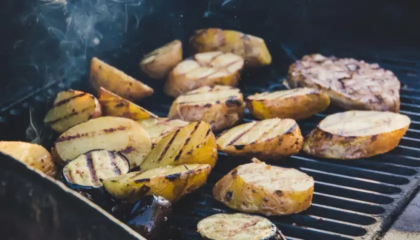 Pommes de terre coupées en quartiers, grillées à la perfection sur un barbecue, dégageant une fumée alléchante. Quelle pomme de terre barbecue !