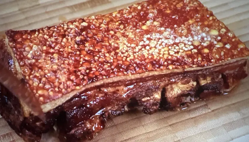 Poitrine de porc barbecue croustillante, avec une couenne dorée et des côtes apparentes, prête à être dégustée sur une planche en bois.