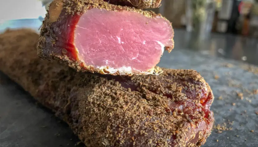 Un morceau de viande séchée, enrobé d'épices, dégage une odeur délicatement boucanée. Sa chair rose vif contraste avec sa croûte brune.
