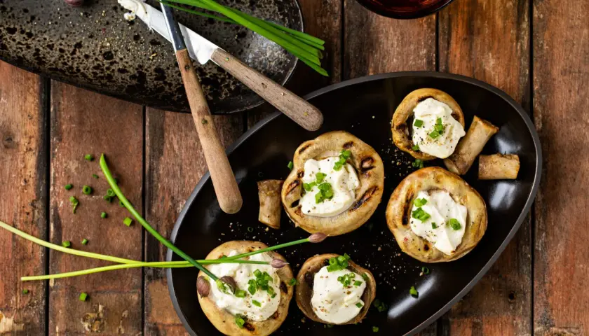 Champignons au barbecue farcis de fromage crémeux et garnis de ciboule fraîche. Un délice simple pour un repas estival.