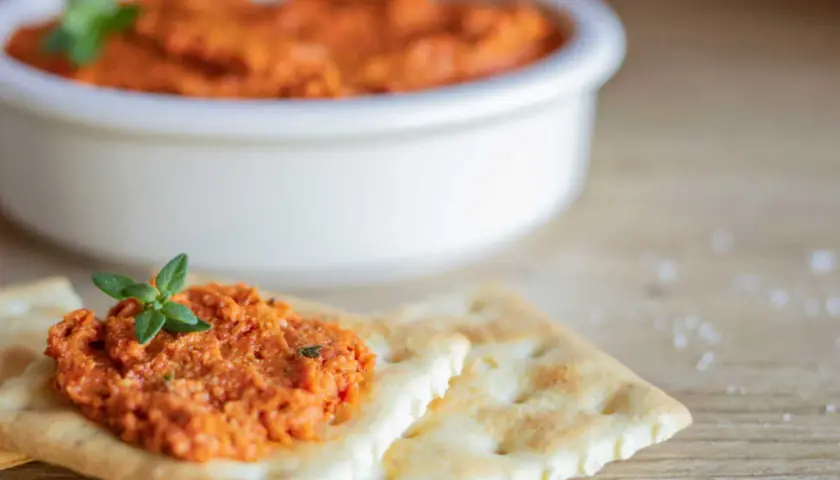 Une cuillère de rillette de chorizo, garnie d'une feuille de persil, sur des crackers. Un bol de cette délicieuse préparation est en arrière-plan.