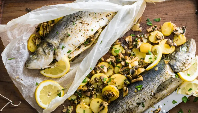 Deux bars en papillote au barbecue, accompagnés de pommes de terre et champignons, citron et persil.