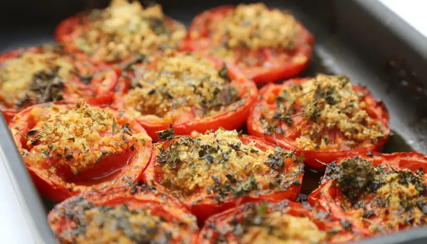 Tomates au barbecue, coupées en deux et garnies d'une chapelure aux herbes, cuites dans un plat.