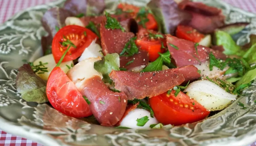 Salade fraîche avec des tranches de fumer magret de canard, tomates, oignons et laitue, parsemée d'herbes.