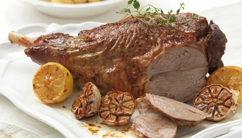 Gigot d'agneau rôti, parfumé au thym, servi avec des citrons grillés et de l'ail confit. Parfait pour une cuisson agneau barbecue réussie.