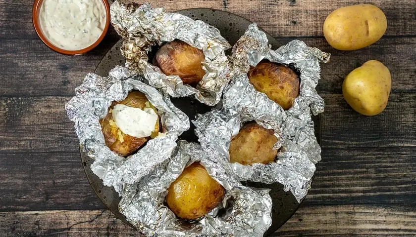 Pommes de terre en papillote sur barbecue, prêtes à être dégustées avec une sauce crémeuse. Le temps cuisson est parfait pour cette recette.