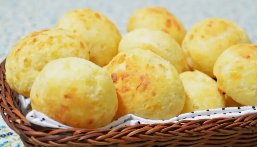 Un panier en osier déborde de délicieux pao de queijo dorés, parfaits pour un goûter.