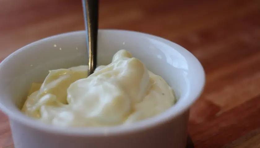 Une cuillère est plantée dans un bol de mayonnaise crémeuse, prête à être dégustée.