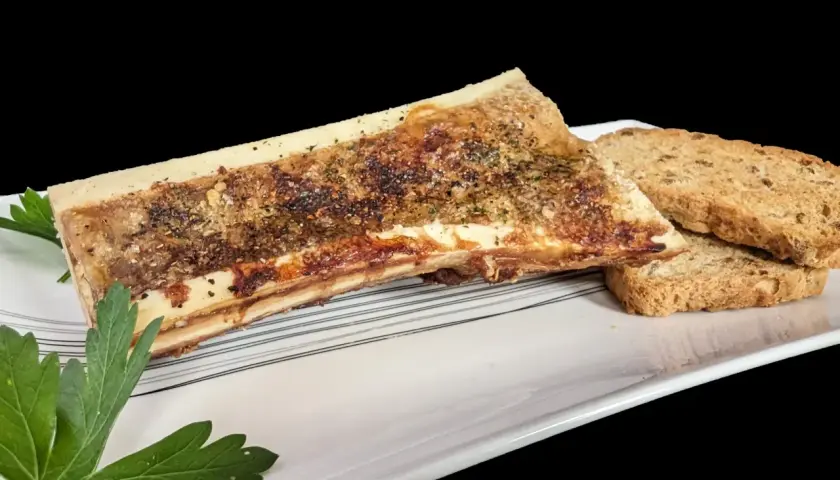 Un os à moelle rôti, assaisonné d'herbes et de poivre, servi avec des toasts croustillants sur une assiette blanche.