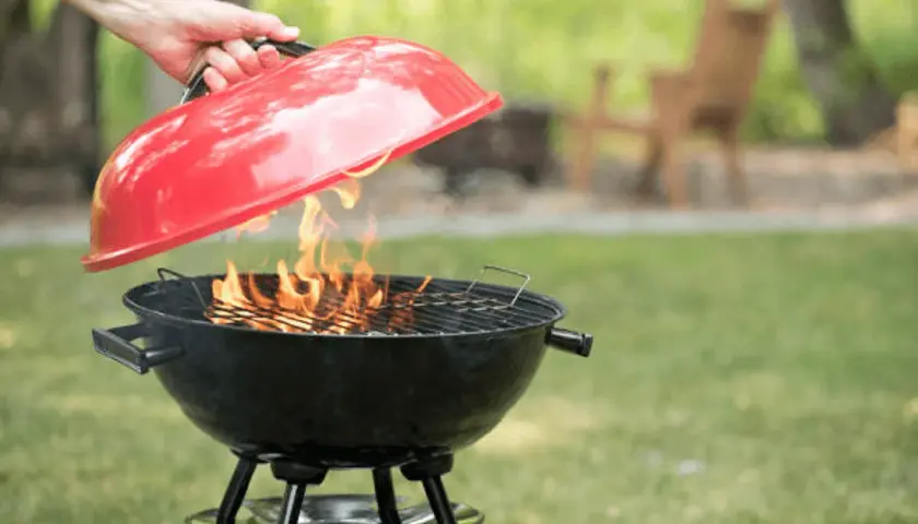 Maintenant, apprenons comment éteindre un barbecue. Une main soulève le couvercle rouge d'un barbecue noir où des flammes dansent.