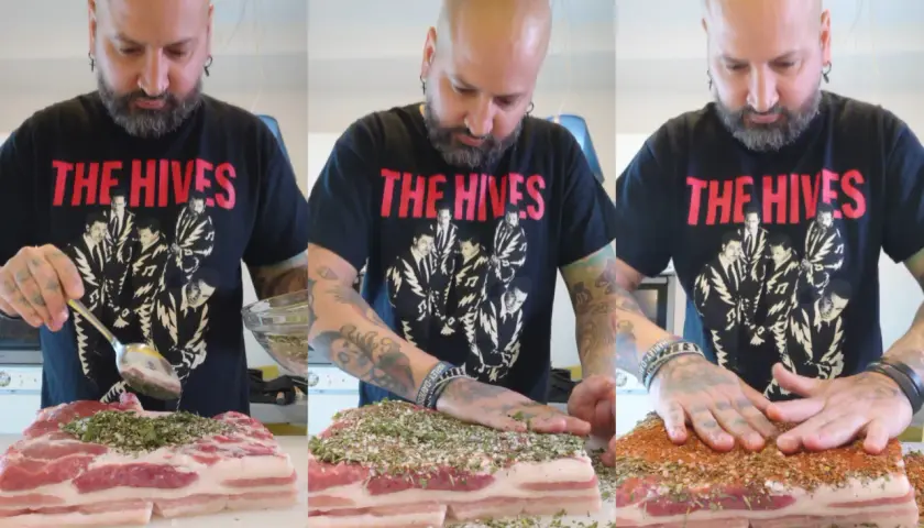 Un homme prépare une recette de poitrine de porc en la saupoudrant d'épices. Il masse la viande avec ses mains tatouées.
