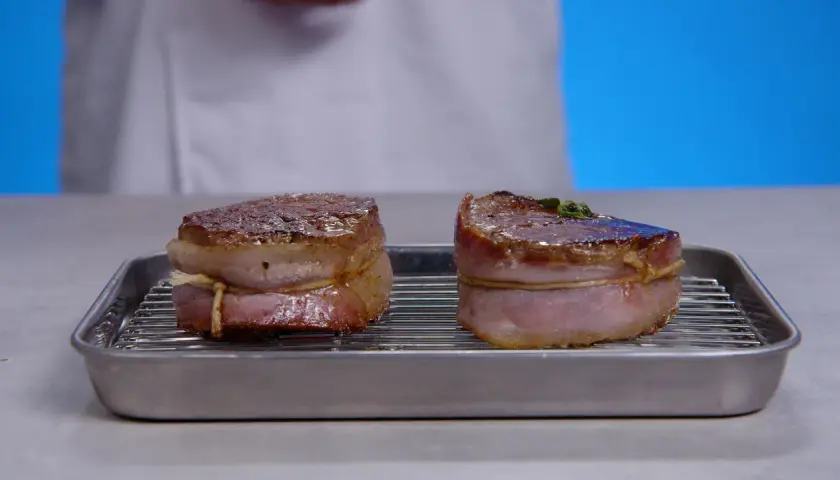 Deux filets mignons au barbecue, enveloppés de lard, reposent sur une grille dans un plat.