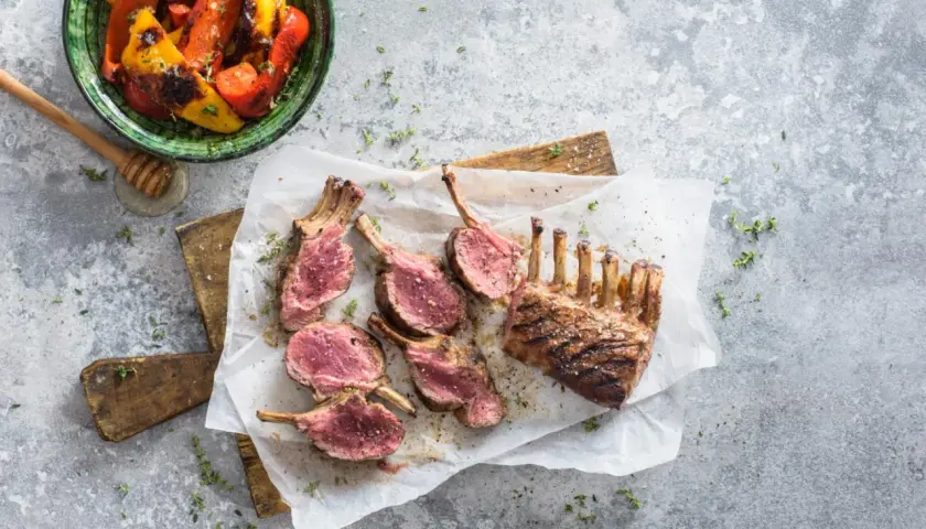 Un délicieux carré d'agneau au barbecue, coupé en côtelettes rosées, servi avec des poivrons grillés.