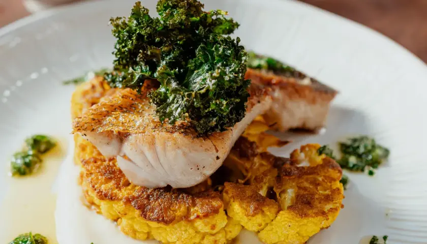 Poisson grillé sur un lit de chou-fleur plancha, garni de kale croustillant et d'une sauce verte.
