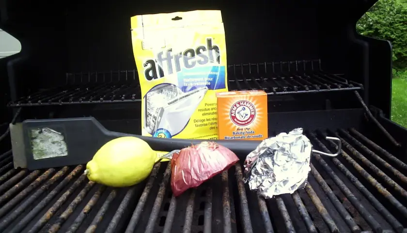 Sur la grille barbecue, un citron, un oignon, du papier aluminium, un nettoyant pour lave-vaisselle et du bicarbonate de soude.
