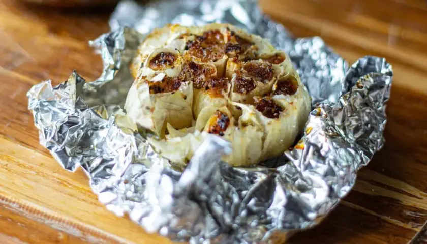Ail au barbecue, rôti à la perfection dans du papier d'aluminium, prêt à être pressé sur du pain grillé.