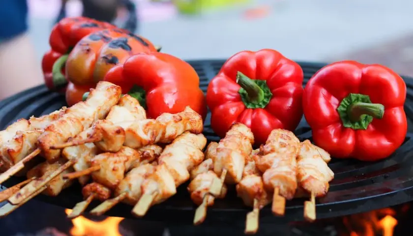 Brochettes de poulet et poivrons rouges sur un barbecue, éclairés par la lumière des flammes.