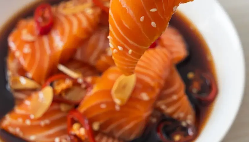 Un morceau de saumon est soulevé d'une marinade foncée avec des piments rouges et de l'ail. Parfait pour une marinade poisson plancha.