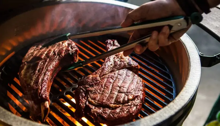 Deux côtes de bœuf savoureuses sur un barbecue à gaz, prêtes pour le temps de cuisson idéal. La chaleur intense des flammes caramélise la viande.