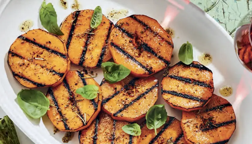 Tranches de courge au barbecue, grillées et assaisonnées, garnies de feuilles de basilic frais. Un délice estival !