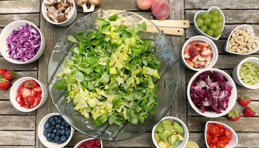 Préparation d'une salade barbecue : laitue, chou rouge, fraises, myrtilles, framboises, avocat, tomates cerises, pêches, raisins, noix de cajou, champignons et chou vert.