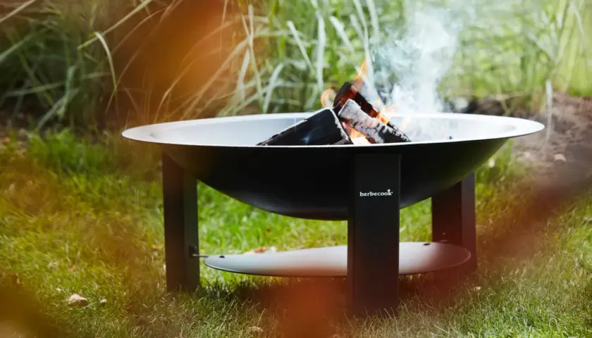 Un brasero Barbecook est prêt à allumer, avec des flammes dansantes et de la fumée s'élevant dans l'air.