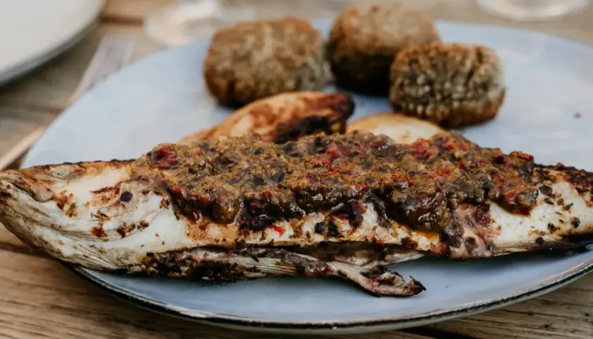 Un loup au barbecue, savamment garni d'une sauce aux herbes et tomates, accompagné de petites boules de pain croustillantes.