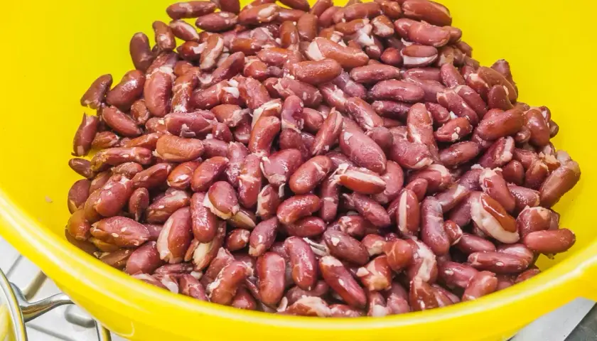 Gros plan sur des haricots rouges dans un bol jaune, prêts pour la cuisson. Ils sont brillants et humides, promettant un plat savoureux.