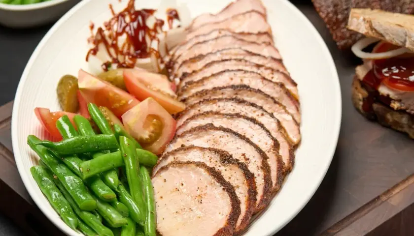 Tranches de longe de porc fumé, accompagnées de haricots verts, tomates, cornichons et oignons. Un délice fumé à savourer.