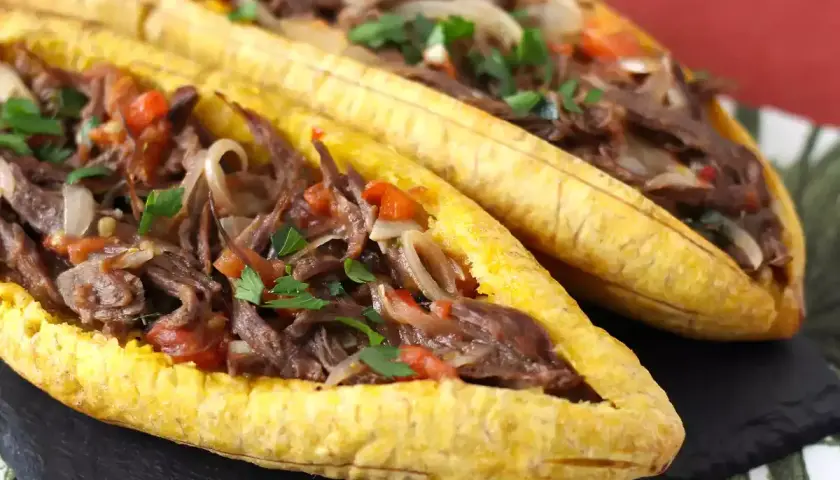 Deux bananes plantain farcies d'un ragoût de bœuf effiloché, d'oignons et de tomates, garnies de persil frais.