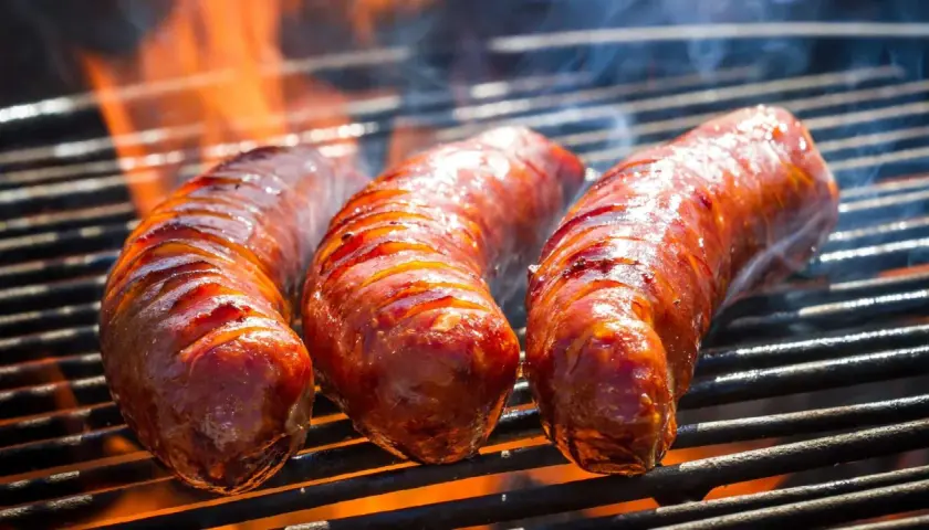 Trois saucisses de bœuf grillent sur un barbecue, leurs jus pétillent sous les flammes. La cuisson saucisse de bœuf barbecue est à son apogée.