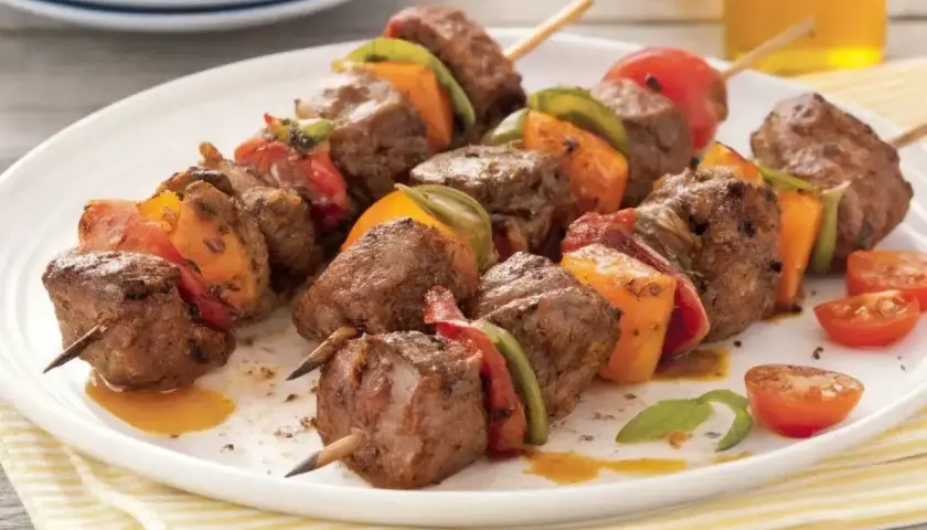 Brochettes de bœuf marinées, garnies de poivrons et tomates, servies sur une assiette blanche.
