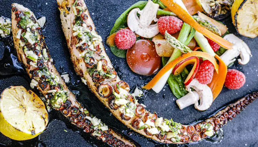 Tentacules de poulpe au barbecue, grillés et garnis d'herbes fraîches, servis avec des légumes croquants et des quartiers de citron grillé.