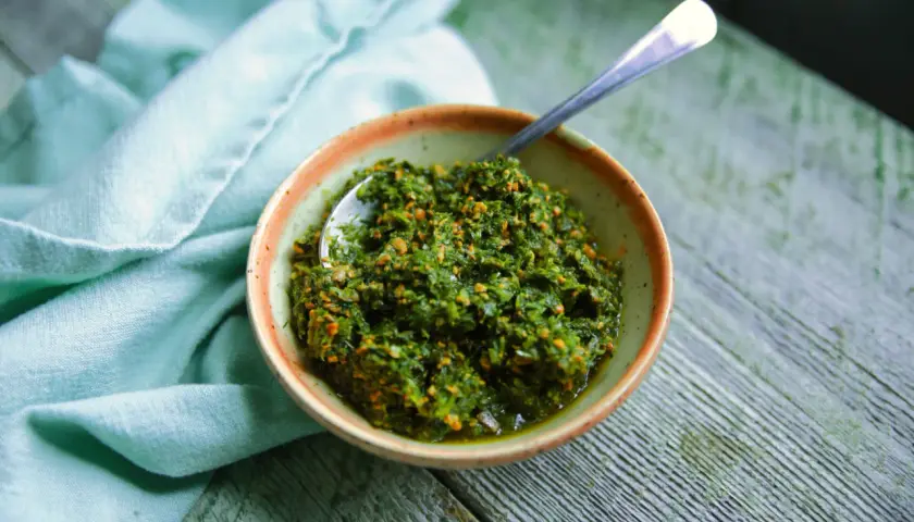 Un bol de pesto de fanes de carottes, prêt à être dégusté, avec une cuillère en argent.