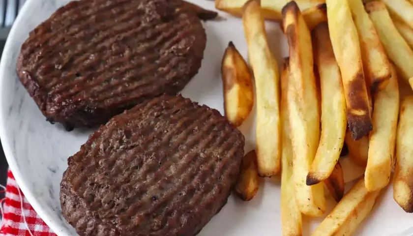Deux steaks hachés au grill électrique, marqués de fines rayures, accompagnés d'une généreuse portion de frites dorées et croustillantes.