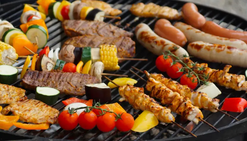 Un festin de Noël en plein air : brochettes de poulet, saucisses, steaks et légumes colorés sur un barbecue.