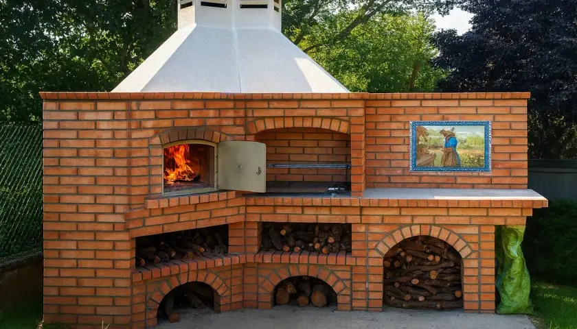 Un grand barbecue en briques, avec un feu qui crépite et du bois rangé, prêt pour un repas rustique au barbecue.