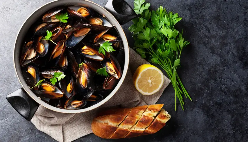 Un plat de moules grillées, garni de persil frais, d'un quartier de citron et d'une baguette à l'ail, prêt à être dégusté.