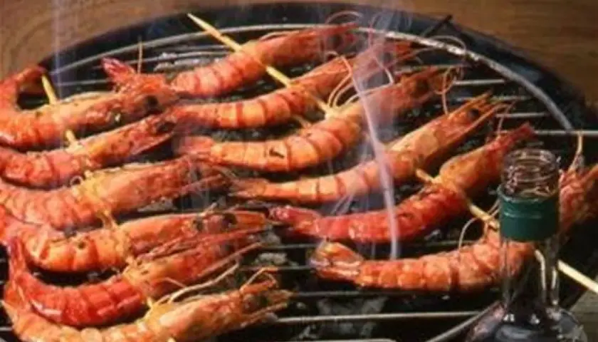 Gambas grillées sur un barbecue, fumantes et appétissantes. Une bouteille de sauce est à proximité, suggérant une délicieuse marinade pour gambas au barbecue.