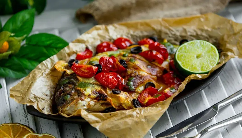 Dorade en papillote au barbecue, garnie de tomates cerises, olives et citron vert. Le temps de cuisson est parfait pour ce plat savoureux.