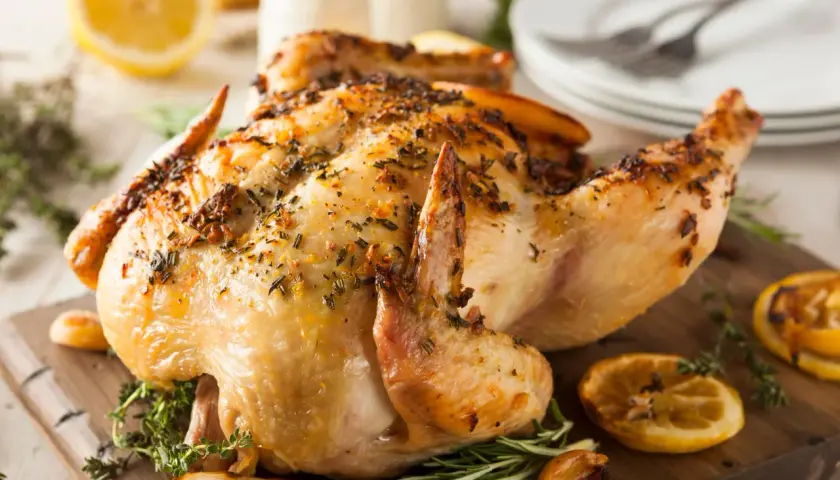 Un délicieux poulet à la broche, doré et savoureux, garni d'herbes fraîches et de quartiers de citron grillés sur une planche en bois.