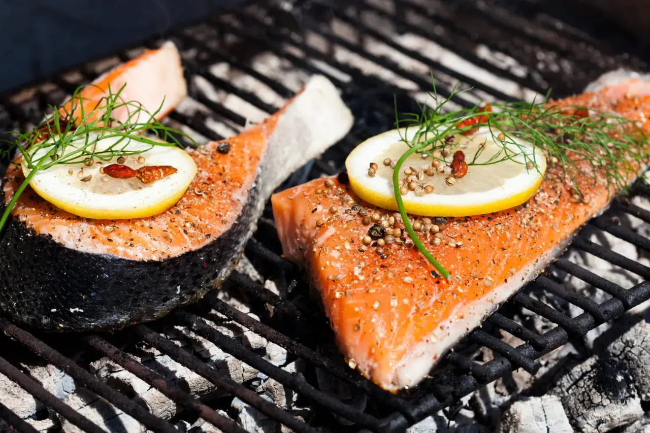 Deux pavés de saumon au barbecue, assaisonnés et garnis de citron et d'aneth, cuisent sur une grille chaude.