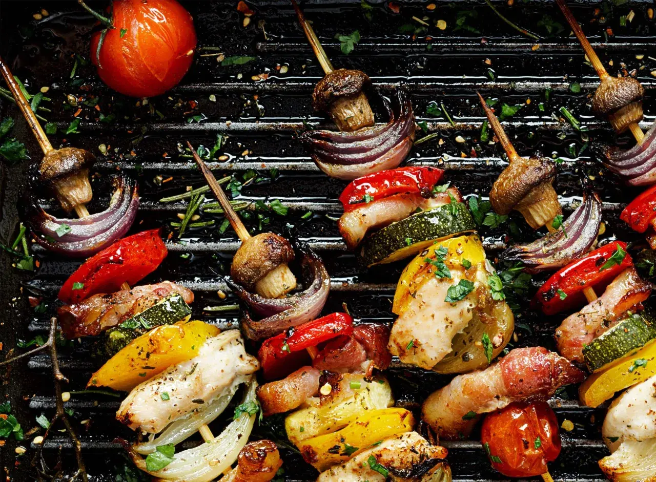Brochettes de poulet et de legume bbq sur un grill, avec des poivrons, courgettes, oignons rouges, champignons et tomates.