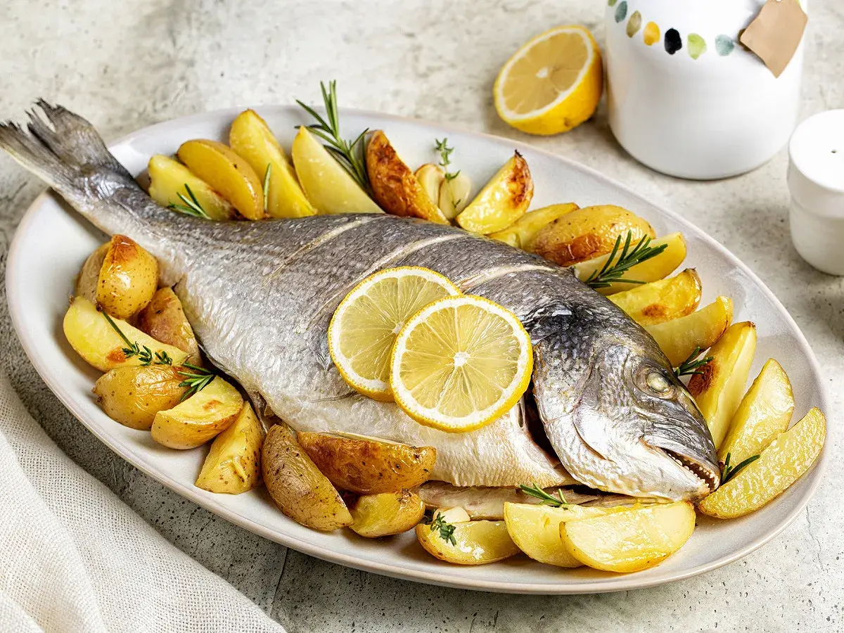 Dorade au barbecue à la portugaise, entière, dorée et savoureuse, accompagnée de pommes de terre rôties et de rondelles de citron.