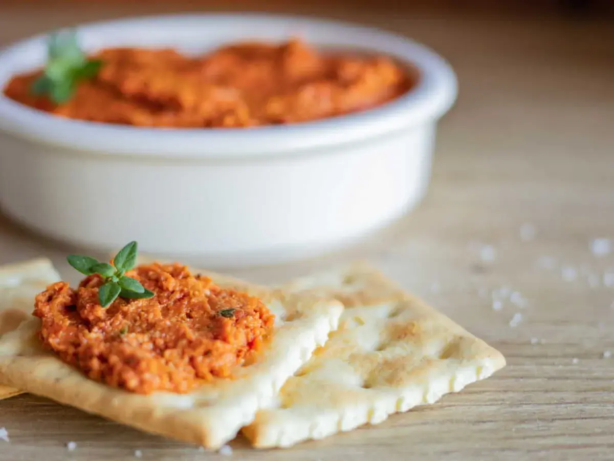Une cuillère de rillette de chorizo, garnie d'une feuille de persil, sur des crackers. Un bol de cette délicieuse préparation est en arrière-plan.