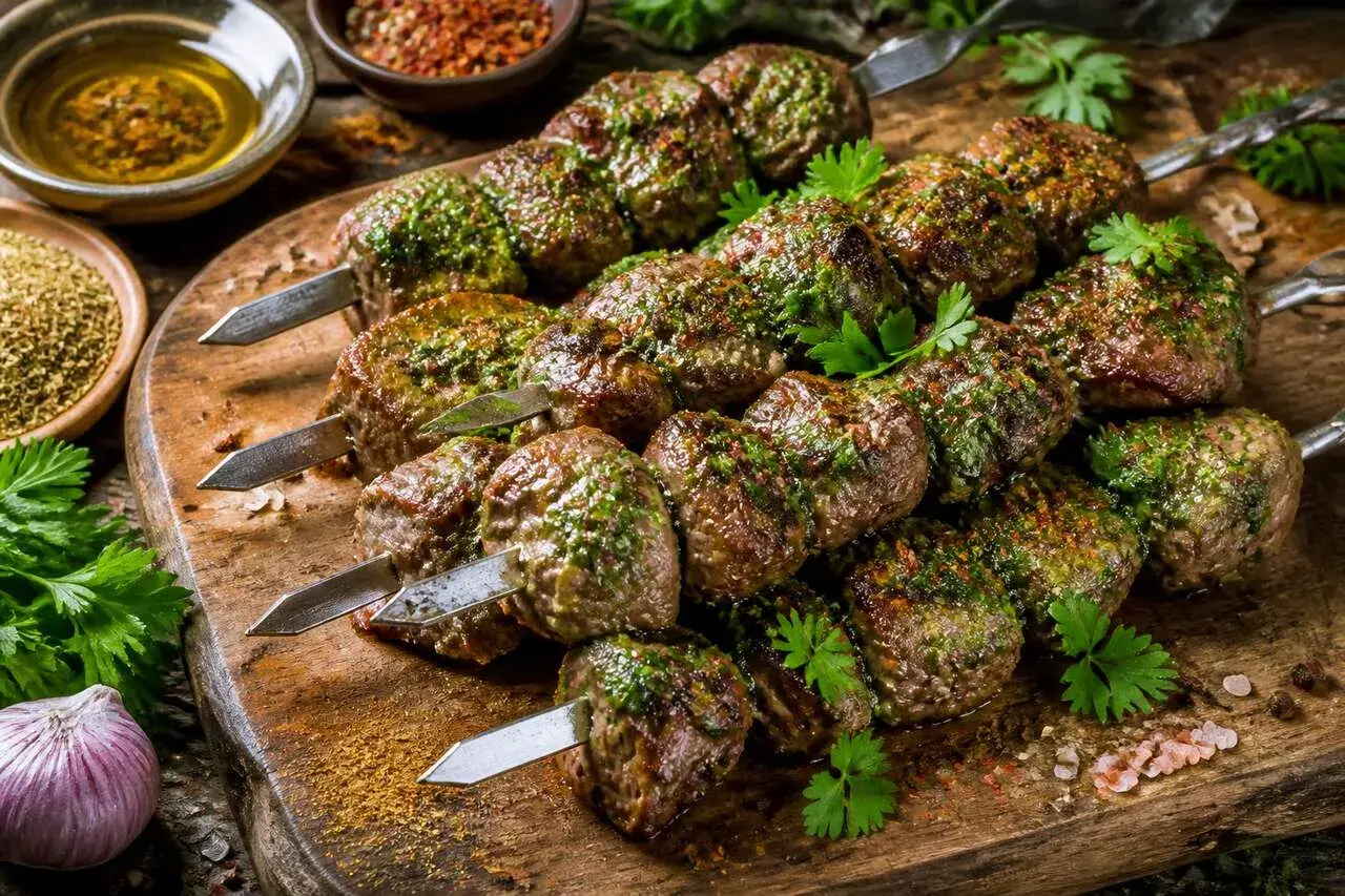 Brochettes d'agneau marinées, prêtes pour la cuisson au barbecue. Herbes fraîches et épices sur fond de bois.